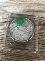 Reverse side of 1966 Canadian Silver Dollar showing a canoe with two paddlers and inscriptions including 1966 and DOLLAR in a plastic protective case.