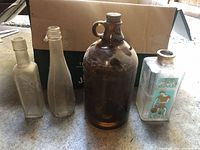 Four individual glass bottles standing upright showing color and shape variety including an amber jug and a decorated square bottle.