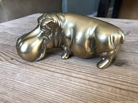 Side view of solid brass hippo figurine showing rounded snout, eye detail, and folds on neck.