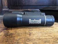 Side view of black Bushnell binoculars showing brand name on the side.