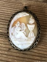 Front view of oval cameo shell pendant/brooch depicting seated woman playing harp beside flaming urn in detailed white relief on orange shell background with ornate metal frame.