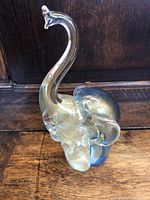 Side view of glass elephant figurine showing curved trunk and blue accents on the body.