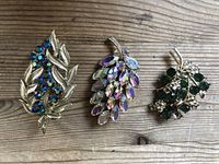 Three vintage costume jewellery brooches displayed on wooden surface with natural light showing colors and condition.