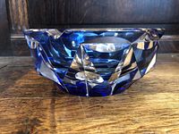 Side view showing blue and clear faceted cut glass design of the ashtray on a wooden surface.