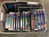 Photo of a plastic bin with various Disney and Star Trek VHS tapes standing vertically.