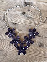 Top-down view of the vintage amethyst gemstone necklace laid flat on a wood surface, showing the floral clusters and chain.