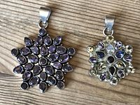 Two gemstone pendants shown on wood surface, one primarily amethyst and one multi-gemstone,