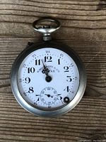 Front view of H. Rosskopf & Co. vintage pocket watch on wood surface showing white dial, black and red numerals, and metal case.