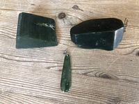 Two rough jade stones and one jade pendant laid out on a wooden surface.