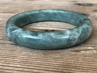 Front angled view of green spinach jade bangle on wooden table.
