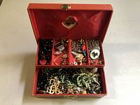 Open red vintage jewelry box showing assorted costume jewelry inside.