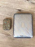 Match Vesta and Cigarette Case side by side on wooden surface, showing size and exterior detail