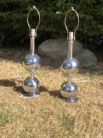 Pair of vintage Mid Century Modern chrome lamps standing on grass outdoors, showing overall condition and design.
