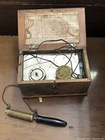 Photo of open wooden box containing metal components and wiring of the vintage No.4 D.D. Home Medical Apparatus with attached probe device.