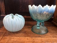 Two opalescent glass items on a wooden surface, showing both the footed dish and the squat pinch vase.