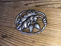 Close up image showing the front of the silver brooch with oak leaf and acorns detail, highlighting the design and wear.