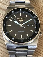 Close-up front view of vintage Seiko 5 automatic wristwatch black dial showing day-date function and silver-tone markers.