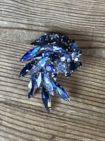 Photo showing front angle of Sherman signed brooch with multiple blue and clear rhinestones arranged in a leaf/flower pattern on wooden surface.