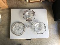 Top view of four crystal bowls with silver overlay and two small glasses on white table.