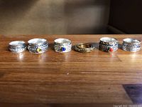 Six rings lined up horizontally showing front pattern, including gemstones and gold-tone ring in center.