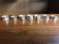 Photo showing full set of seven silver rings arranged in a row on wooden surface, highlighting various designs and stone settings.