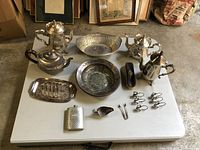 Angled view showing details of silver plated teapots, bowls, trays and smaller items on white table.