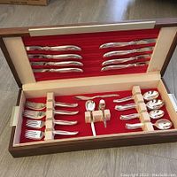 Full view of open wooden case displaying all flatware pieces against red felt background