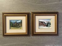 Two framed miniature paintings side by side; forest and snowy cabin scenes.
