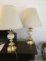 Two table lamps placed on a dark surface, showing overall appearance with white pleated shades and white and gold bases.
