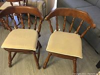 Two vintage Windsor style wooden chairs with beige cushions, showing the front and top views of the seats, spindled backs, and turned legs on wood flooring.