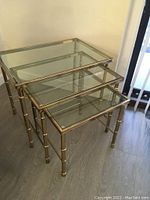 Full view of all three vintage brass nesting tables with glass tops, stacked inside each other. Shows brass frames and faux bamboo legs.
