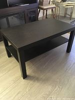 Side view showing black coffee table's flat top surface and rectangular legs with a lower shelf underneath.