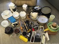 Overview of various kitchenware items including coffee maker, pots, CorningWare dishes, bowls, utensils, and small appliances on floor.