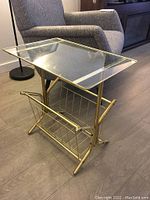 Full side view of the glass top table with brass tubular frame and brass magazine rack below.
