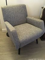 Front view of gray upholstered chair showing seat, backrest, armrests and front legs