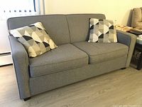 Full front view of grey upholstered sofa bed couch with two geometric throw pillows