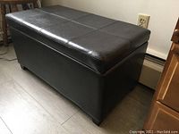 Side view of closed black faux leather storage bench with stitched detailing on top and block feet.