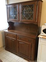 Full view of vintage wooden hutch with stained glass cabinet doors and wood lower cabinets with drawers.
