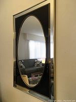 Full face image of the vintage large mirror showing oval reflective surface, black and gold trim around the oval with silver metallic outer frame.