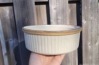 Side view of off-white stoneware dish with ribbed vertical lines and brown rim.