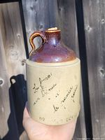 Front view of antique whisky crock jug showing two-tone glazed ceramic with inscription and cork stopper.