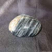 Dark black mineral specimen with white striations on a dark fabric background.