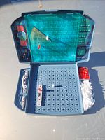 Retro Battleship board game setup with blue grid, plastic ships, and storage compartments for pegs and pieces