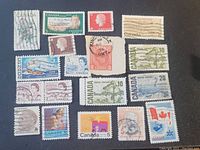 Top-down photo of 17 assorted used Canadian postage stamps laid out loosely on black background.