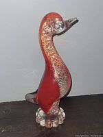 Front and side view of the red Murano glass duck sculpture with silver flake inside, standing on a clear sculpted glass base shaped like feet.