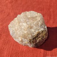 Crystal mineral specimen with visible rough beige/brown translucent crystals on red fabric background.
