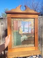 Full view of mixed media painting showing a yellow bird figure sitting indoors by window with outdoor scenery, framed in carved pine wood frame with decorative top.