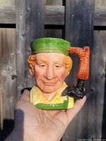 Front view of vintage ceramic Toby mug showing character face, green hat, and boot handle