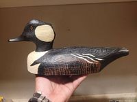 Front and side views of the hand-carved duck decoy with detailed paintwork showing black, cream, and brown colors.