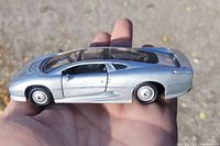 Side view of silver Jaguar XJ220 die cast model car held in hand, showing sleek aerodynamic design, clear windows, and overall condition.
